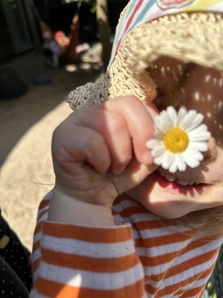 Kind hält sich ein Gänseblümchen vor das Auge
