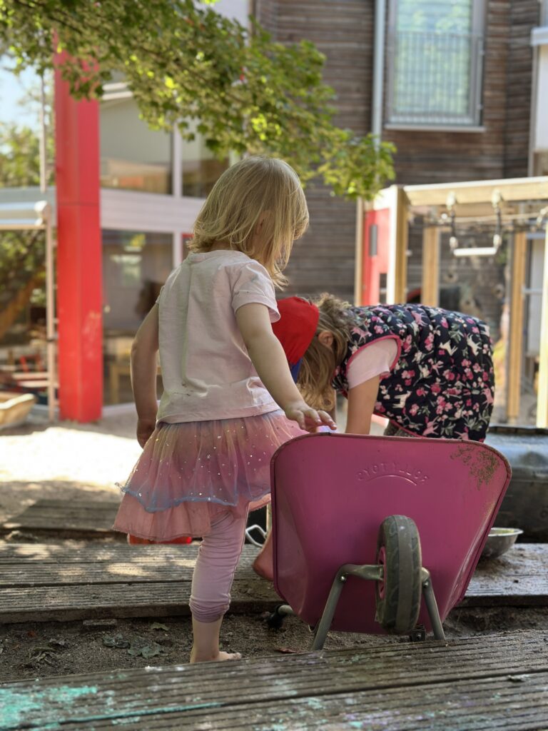 Kinder spielen mit rosa Schubkarre