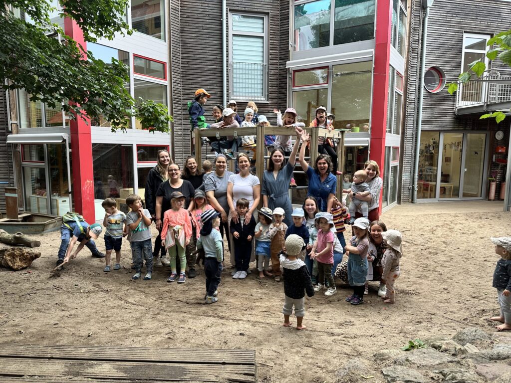 Gruppenfoto von jubelnden Kindern und Fachkräften vor Klettergerüst